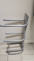 Side angle view of silver metal rack with four horizontal arms designed to hold water bottles.