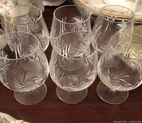 Six crystal cognac glasses in a set, showing etched pine needle design and overall shape, with details of clarity and condition visible.