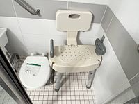Assistive toilet and shower chair positioned next to toilet with bag of small accessories on toilet lid.