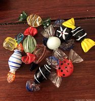 Top-down view of 10 Murano glass candy figurines in various colors and patterns on wood surface
