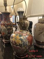 Front angle showing hand painted floral ceramic vase lamp with brass fixtures and wooden base.
