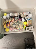 Bin with golf balls of various colors and brands, including tees, ball markers, two boxes of Callaway golf balls, and a magnetic mini tee counter set.