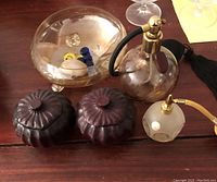 Photo taken showing round and smaller hexagonal perfume bottles with gold atomizers, two wooden pumpkin jars, and glass bowl.