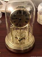 Full view of Seiko clock inside glass dome with gold-tone details.