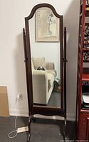 Full view of dark wood framed cheval mirror with an arched top and spindle side supports, standing on curved legs.