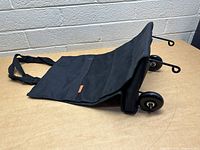 Side view of the black collapsible bag with wheels laid on its side showing mesh pocket and wheels.