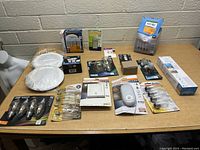 Image showing an assortment of lighting items arranged on a wooden table including ceiling light fixtures, LED light bulbs, motion sensor light, floodlight bulbs, dimmer switch, and electrical connectors.