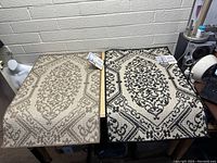 Two decorative floor mats laid out on desks, showing one beige and one black & cream mat with intricate medallion patterns.