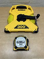 Both DeWalt tape measures visible: large 300-foot tape with crank handle and smaller 35-foot tape measure on table.