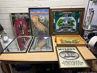 Seven assorted bar mirrors displayed on a table against white wall, showing different brands and graphics.