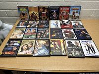Photo showing 22 assorted DVDs arranged in rows on a desk, visible titles include You Don't Mess with the Zohan, The Scorpion King, Ladder 49, The Hangmans Curse, The Incredibles, Joe Dirt, and others.
