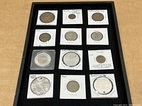 Overview of 12 assorted tokens in cardboard holders arranged in a black tray.