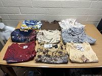 Photo of nine assorted women's tops and hoodies laid flat on table, showing variety of colors and prints, all new with tags.