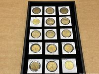 Tray of 12 gold-toned Paris collectible tokens in individual holders with handwritten landmark labels.