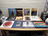 Front view of 12 vinyl record albums laid out on table, showing artist and album cover details.