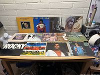 Table with 11 vinyl LP record album covers displayed, showing artists such as Harry Chapin, Doug Kershaw, Rocky, and others, arranged in two rows