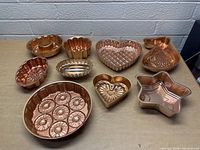 Full view of all ten copper molds arranged on table showing shape variety and patterns.