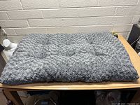 Top view of gray tufted plush dog bed on wooden table showing size and texture.