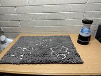 Gray textured pet rug with white paw prints placed flat on a surface next to blue and white PetSafe automatic pet feeder dispenser with black base