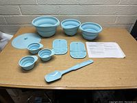 Photo showing all items including four collapsible bowls of varying sizes, three measuring cups, two pot holders, a spatula, a lid, and instruction sheet arranged on a table.