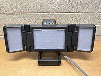 Front view of Ridgid work light showing three LED panels: one big center panel and two foldable side panels with LED bulbs.