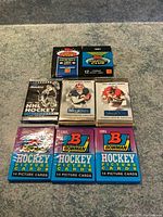 Eight sealed hockey and football card packs from 1991 and 1992 of Pinnacle, Topps Stadium Club, Bowman, SkyBox brands arranged on carpet.