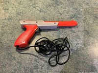 Front angle of Nintendo Zapper light gun showing cable and connector, lying on carpet.