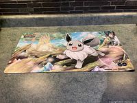 Top view showing the full playmat with Eevee on a fantasy nature background with prominent Pokémon logos