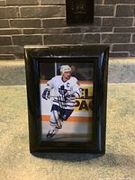 Framed Wendel Clark autographed hockey photograph showing player in action on ice with black autograph signature.