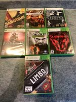 Seven Xbox 360 game cases arranged in two rows, titles visible including The Saboteur, Mercenaries 2, Riddick, Fable II, Splinter Cell Double Agent, Splatterhouse, Limbo/Trials HD triple pack.