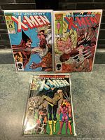 Three issues of The Uncanny X-Men comics displayed: issue 167 with Wolverine vs Sabretooth cover, issue 213 with character cover, and issue 222 with mystical face cover.