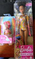 Photo showing two Barbie dolls in original packaging: a gymnast doll in colorful leotard and a smaller pink-haired doll.