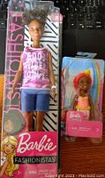 Two Barbie dolls in original retail packaging, one a Barbie Fashionistas doll and one a smaller Barbie doll, both new in boxes.