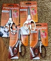 Set of 3 Fiskars scissors with baseball-themed polymer handles in brown and white, each in original packaging showing pointed-tip safety-edge blades designed for children ages 4 and up. Packaging also features an apple logo and warranty details.