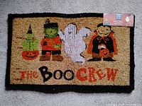 Full view of the rectangular Halloween door mat showing the design with witch, Frankenstein monster, ghost, vampire and text 'The Boo Crew'.