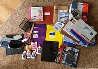 Overview of all miscellaneous office supplies including label maker, glue bottles, scissors, pens, papers, binders, tape, and organizers.