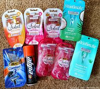 Nine new shaving and wash items on carpet: Bic Soleil Smooth and Comfort 3 disposable razors, Edge shaving gel can, Skintimate razors