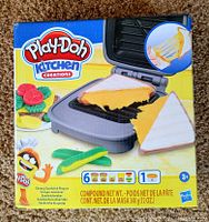 Front view of unopened Play-Doh Kitchen Creations Cheesy Sandwich Playset box showing sandwich grill and six cans of Play-Doh compound.