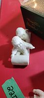 Two white porcelain Snowbabies figurines sliding on sleds blocking view of box with title "My Favorite Snowbabies"