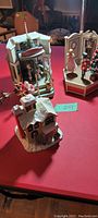 Three Christmas-themed vintage music boxes on a red surface: a toy shop scene with Santa and nutcracker figures, a snow-covered house with winter figures, and a third scene with dancing figurines and Christmas tree.