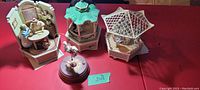 Full view of four Enesco seasonal music boxes arranged on a red surface showing detailed seasonal and architectural themes.