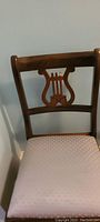 Front view of wooden chair showing harp cutout backrest and upholstered seat with blue fleur de lis fabric