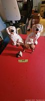 All four Beswick porcelain figurines displayed on red surface: two white fireplace dogs, one brown donkey, one cat.