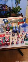 Photo of assorted Christmas figurines, mini lights box, crocheted snowflakes, and other holiday decorations arranged on a table.