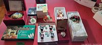 Full lot overview showing the 12 assorted Christmas decorations in boxes and arranged on a red surface