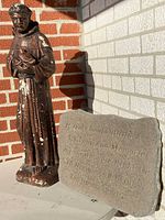 Photo of concrete Saint Francis of Assisi statue with visible paint peeling, next to a concrete stone with an engraved poem