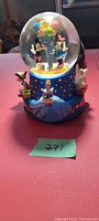 Front view of the musical water globe showing Minnie Mouse and Mickey Mouse with balloons inside the globe, Cinderella and Pinocchio figurines on the base.