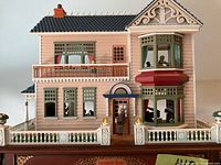 Exterior front view of two-story pink and green vinyl Victorian dollhouse with ornate trim, porch and balcony