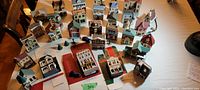 Multiple rows of 37 miniature village buildings including houses and commercial storefronts in pastel and earth tone colors, arranged on a table for viewing.