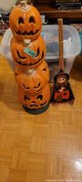 Stack of four orange plastic jack-o'-lantern pumpkins with carved faces in light-up electric decor format seen next to the wooden broom.